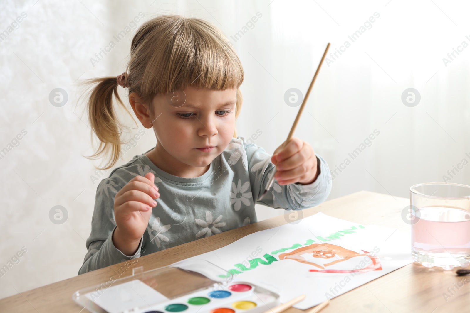 Photo of Cute little girl drawing with brush at wooden table indoors. Child`s art