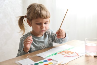 Cute little girl drawing with brush at wooden table indoors. Child`s art