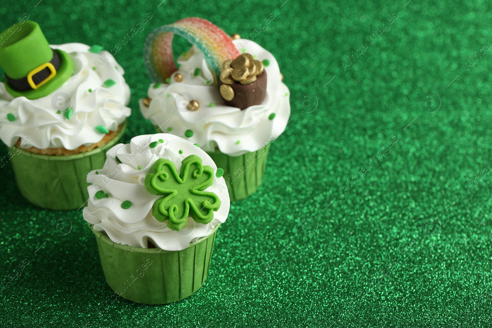 Photo of St. Patrick's day party. Tasty festively decorated cupcakes on shiny green surface, closeup. Space for text