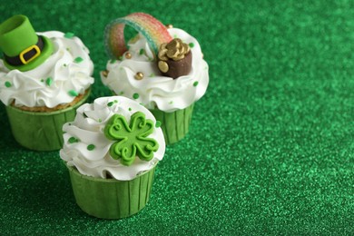 St. Patrick's day party. Tasty festively decorated cupcakes on shiny green surface, closeup. Space for text