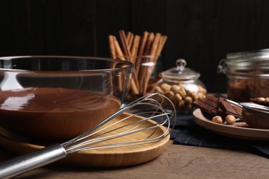 Photo of Bowl of chocolate cream with whisk and ingredients on wooden table