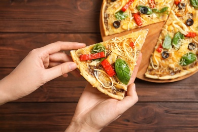 Photo of Woman holding delicious homemade pizza slice on wooden background