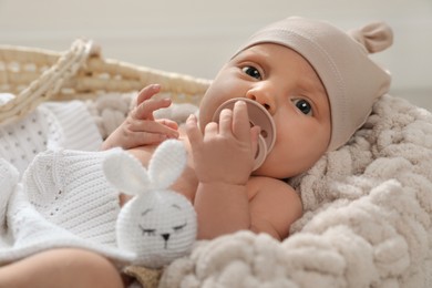 Photo of Adorable newborn baby with pacifier and toy in wicker basket indoors