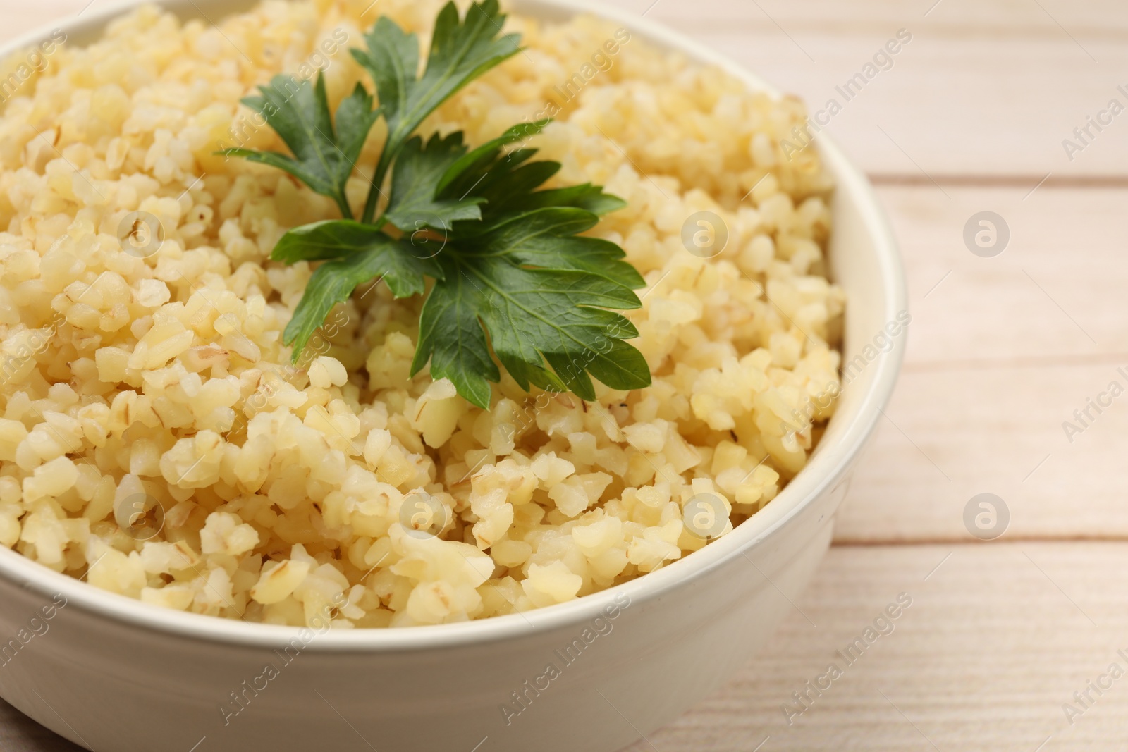 Photo of Delicious bulgur with parsley in bowl on table, closeup