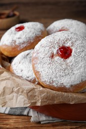 Delicious donuts with jelly and powdered sugar in baking dish on wooden table, closeup