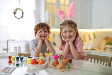 Painting Easter eggs. Cute children with bunny ears at white marble table in kitchen