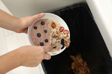 Photo of Woman throwing oatmeal with berries into bin indoors, closeup