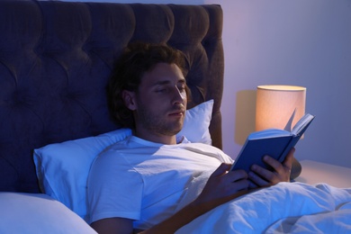 Handsome young man reading book in dark room at night. Bedtime