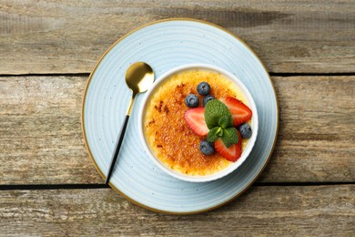 Delicious creme brulee with berries and mint in bowl on wooden table, top view