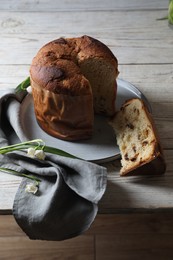 Photo of Delicious cut Panettone cake and beautiful flowers on light wooden table. Traditional Italian pastry