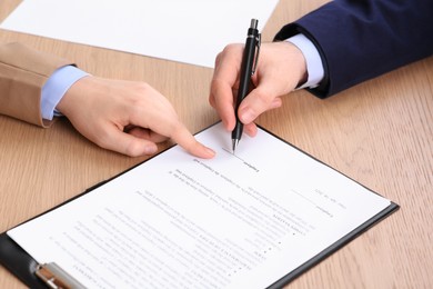 Businesspeople signing contract at wooden table, closeup of hands