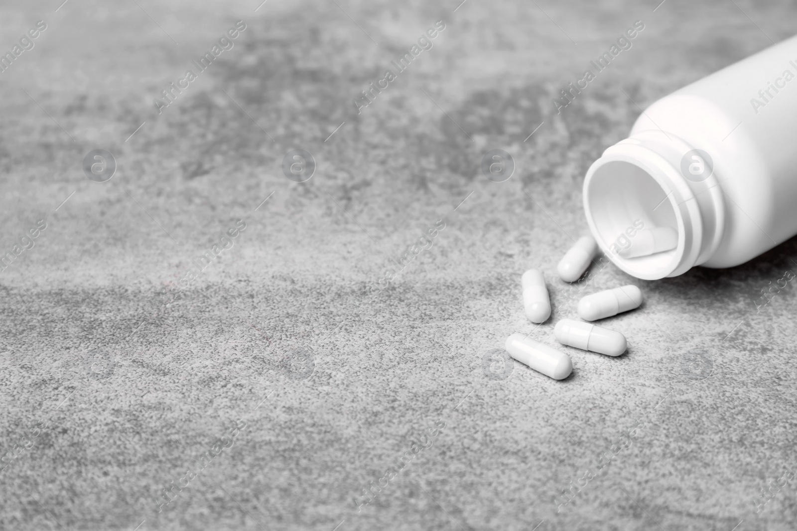 Photo of Container with white pills on grey background