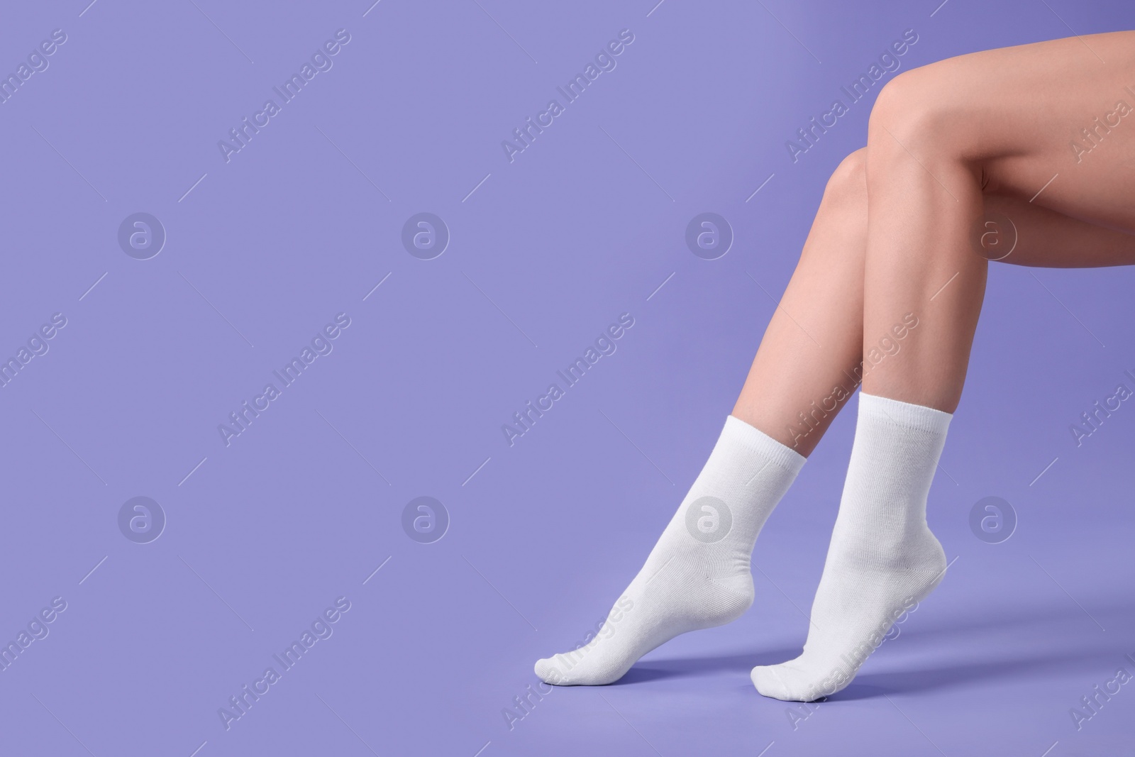 Photo of Woman in stylish white socks on violet background, closeup. Space for text