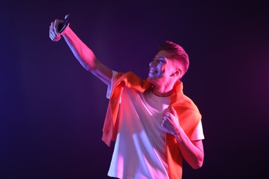 Young man taking selfie on dark background in neon lights