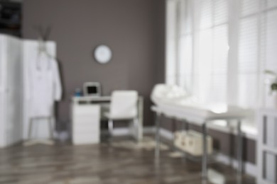 Photo of Blurred view of modern medical office with doctor's workplace and examination table. Interior design