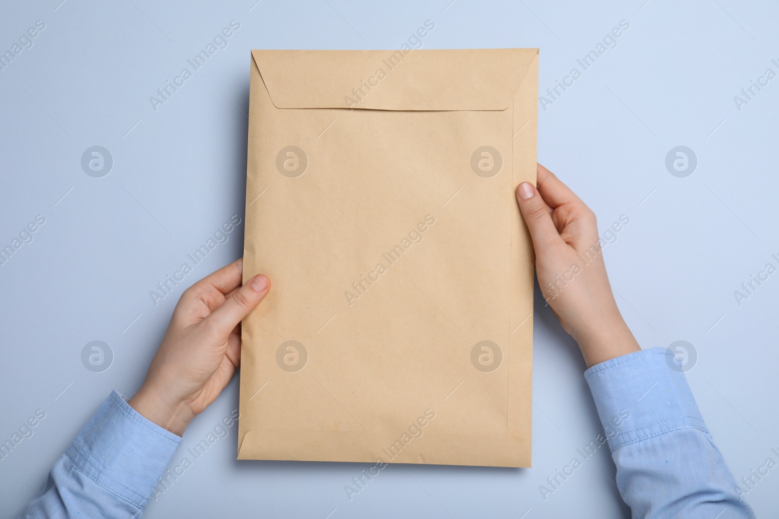 Photo of Woman with kraft paper envelope on light grey background, top view