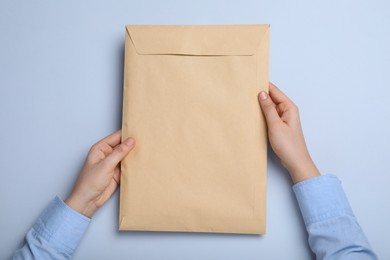 Woman with kraft paper envelope on light grey background, top view