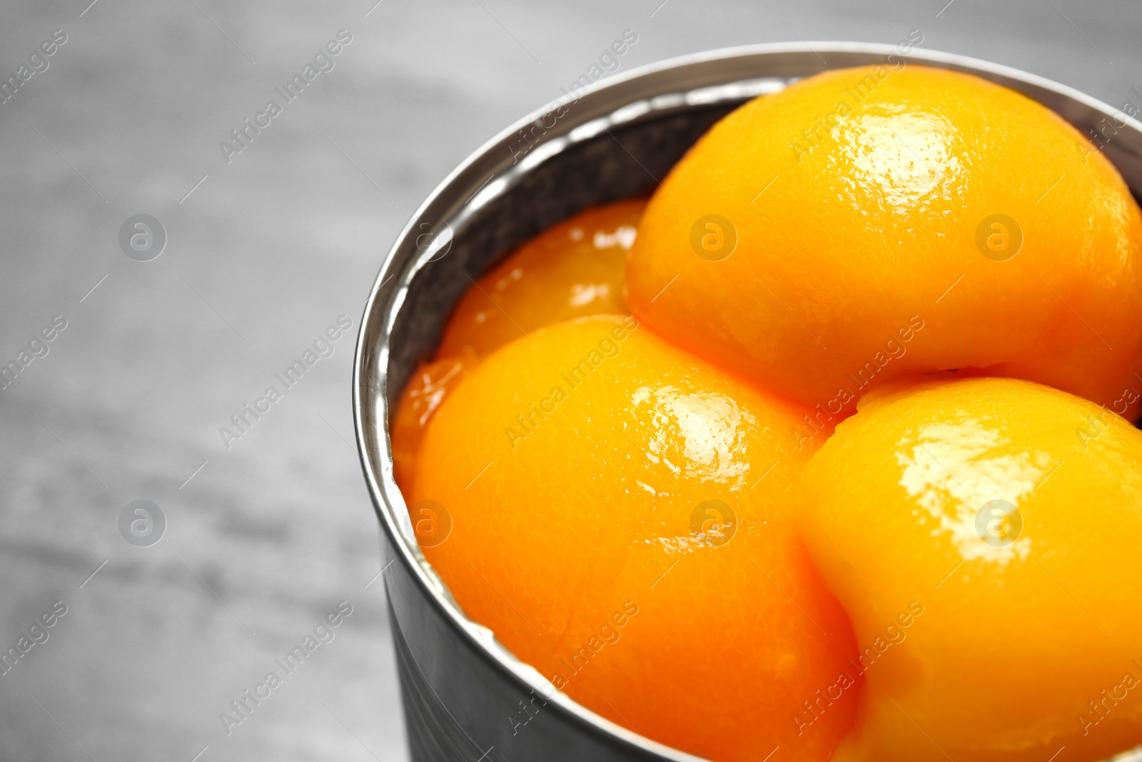 Photo of Open tin can of peaches on grey background, closeup. Space for text