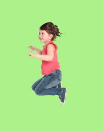 Happy cute girl jumping on light green background