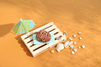 Brain made of plasticine on mini wooden sunbed under umbrella against orange background