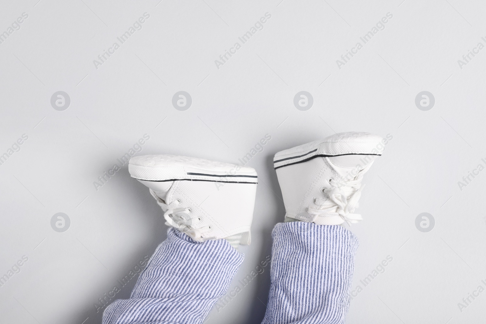 Photo of Little baby in stylish gumshoes on light grey background, top view. Space for text