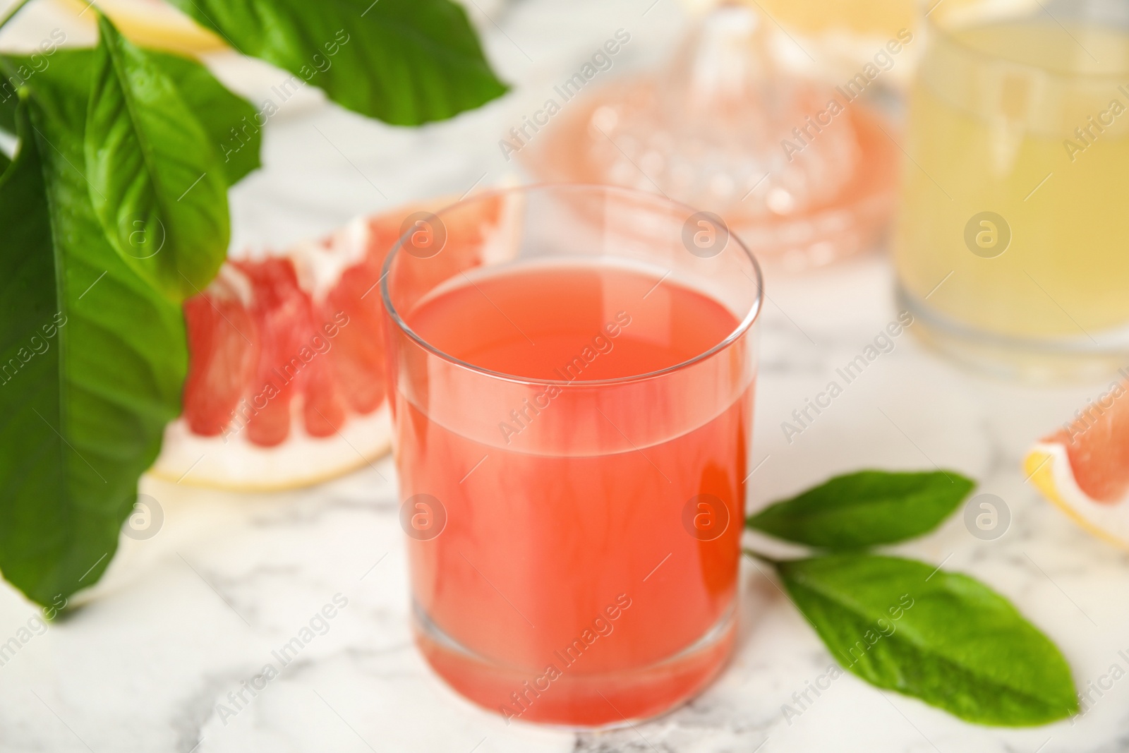 Photo of Glass of pink pomelo juice with green leaves on white marble table, closeup