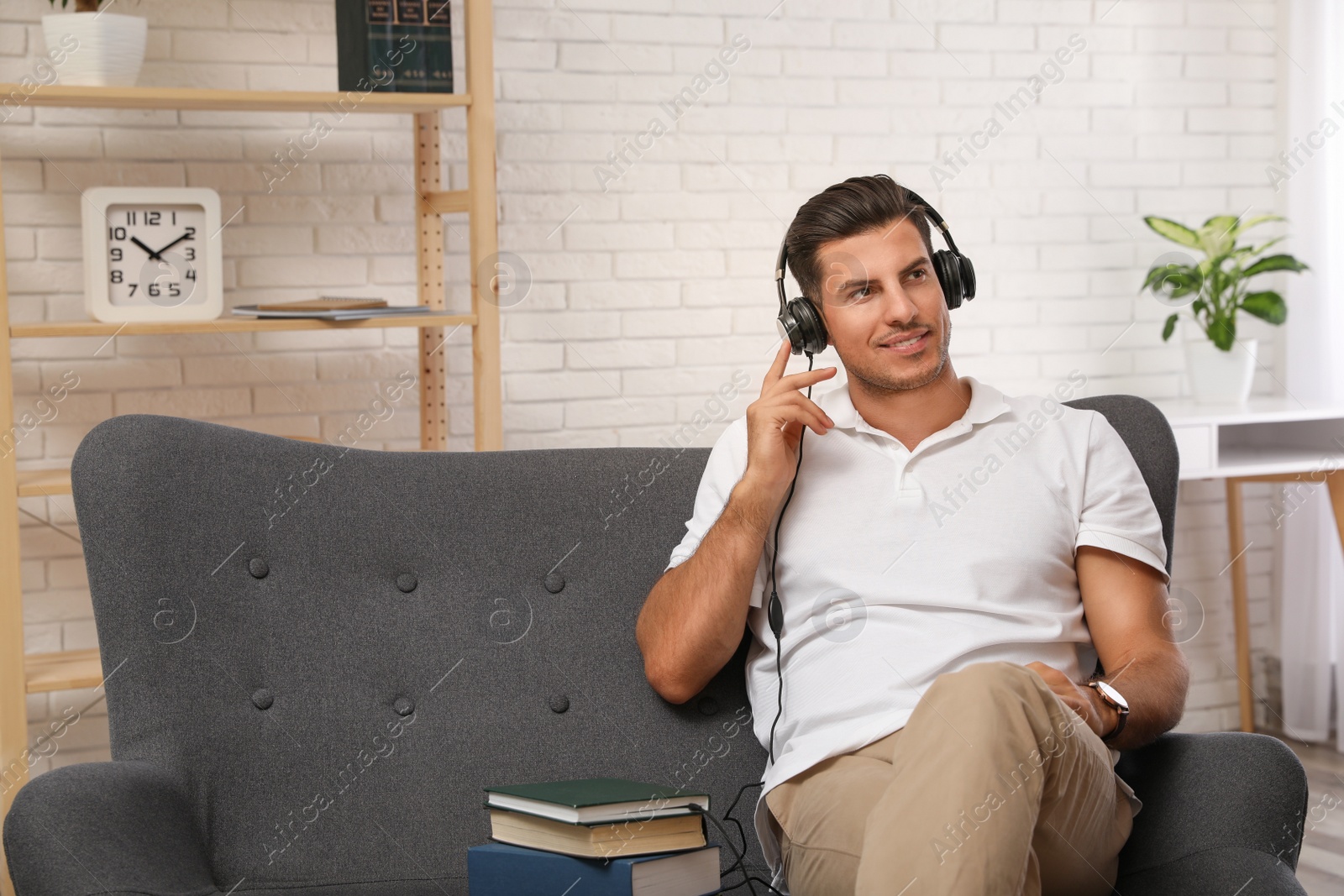 Photo of Man with headphones connected to book
on sofa at home. Audiobook concept