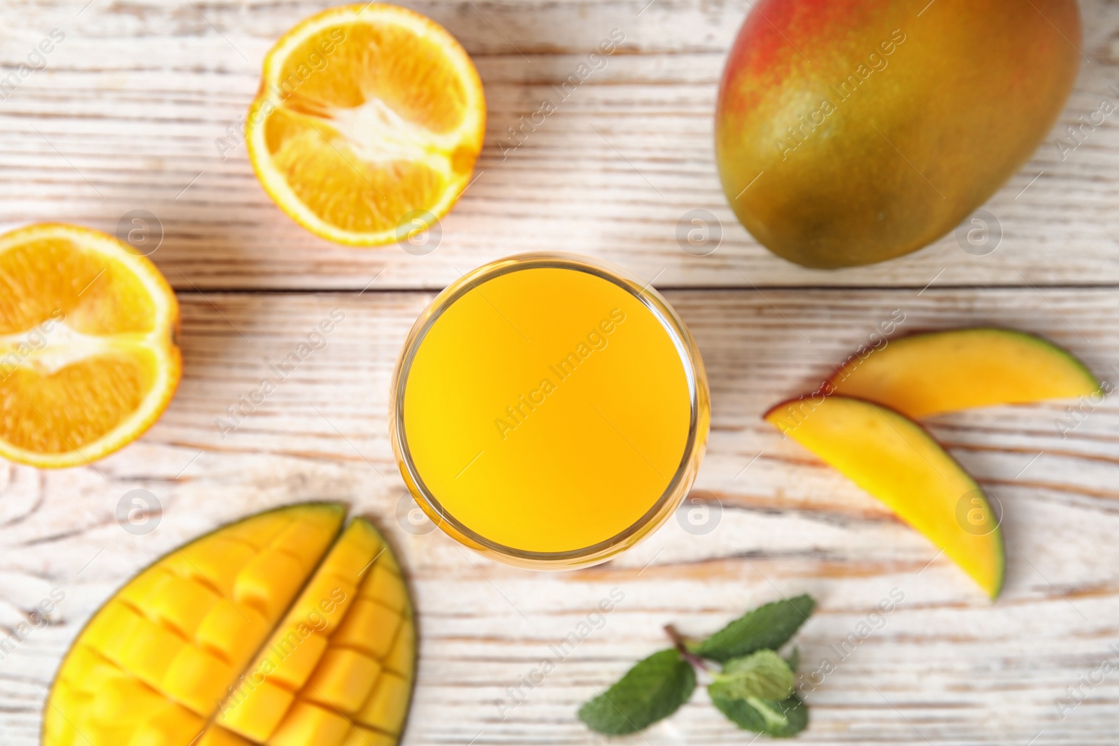 Photo of Glass with fresh mango juice and tasty fruits on wooden table, flat lay