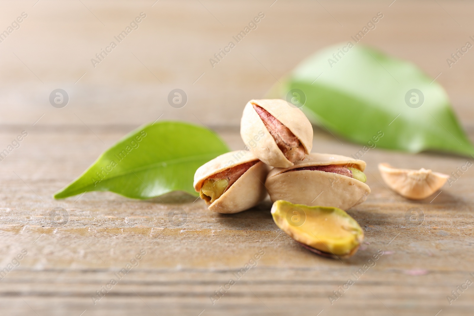 Photo of Tasty pistachios and leaves on wooden table, closeup. Space for text