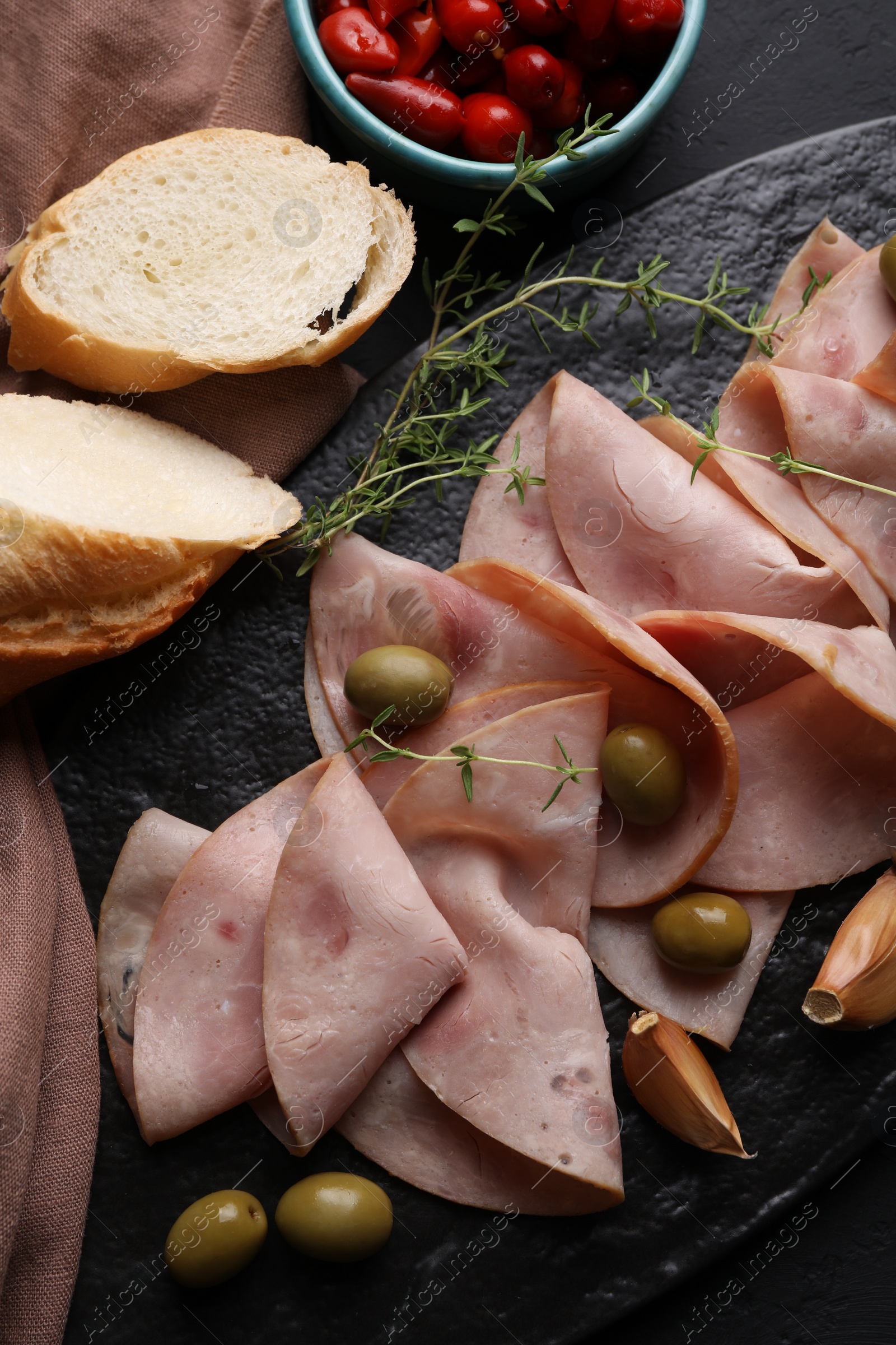 Photo of Tasty ham with olives, garlic, bread and pickled peppers on black table, flat lay