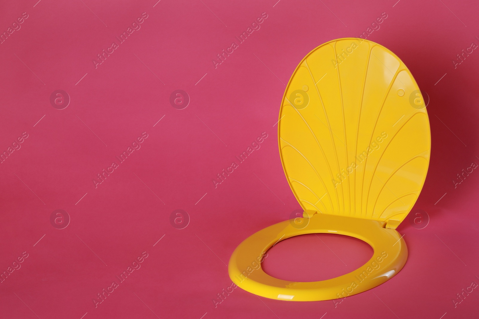 Photo of New yellow plastic toilet seat on pink background, space for text