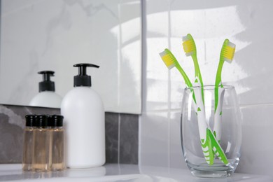Photo of Glass holder with light green toothbrushes in bathroom