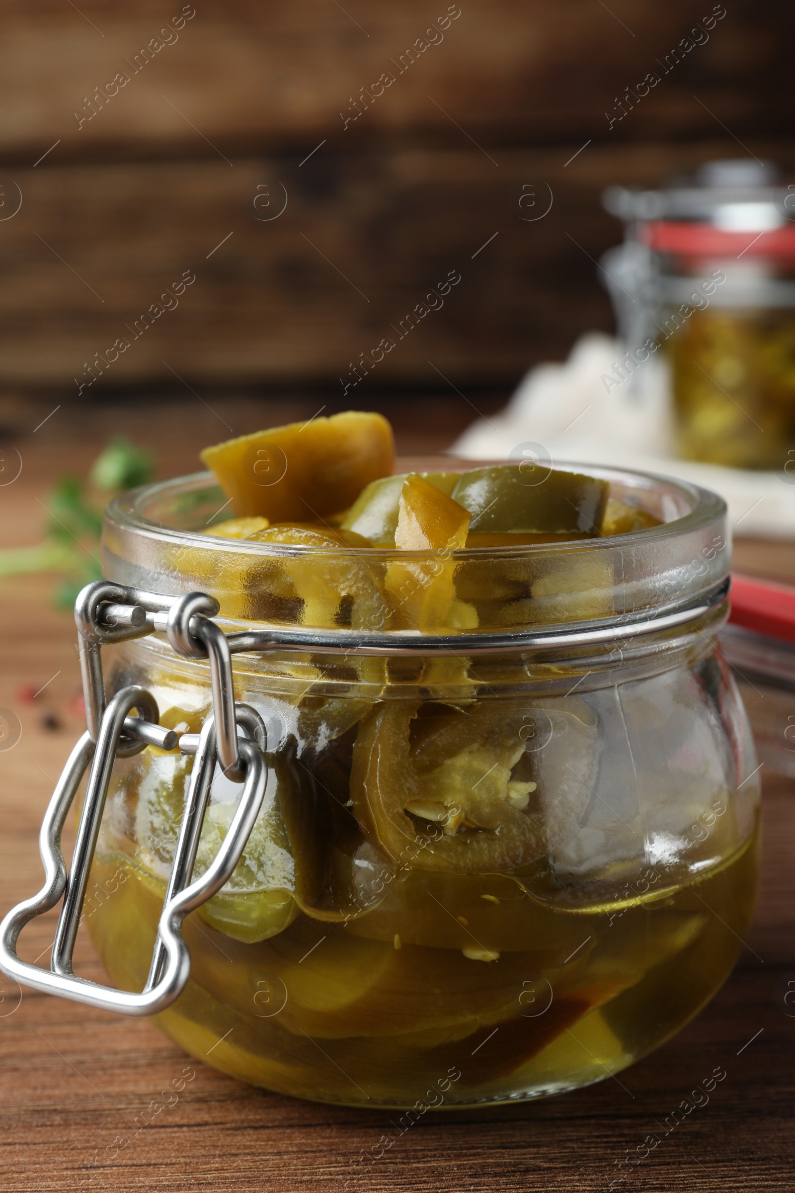 Photo of Glass jar with slices of pickled green jalapeno peppers on wooden table