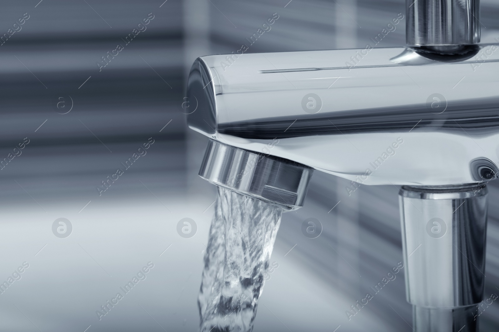 Photo of Water flowing from bath tap on blurred background, closeup