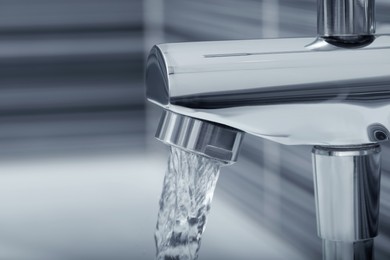 Photo of Water flowing from bath tap on blurred background, closeup