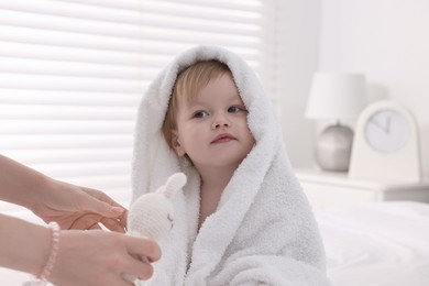 Mother wrapping her cute little baby with towel after bathing on bed