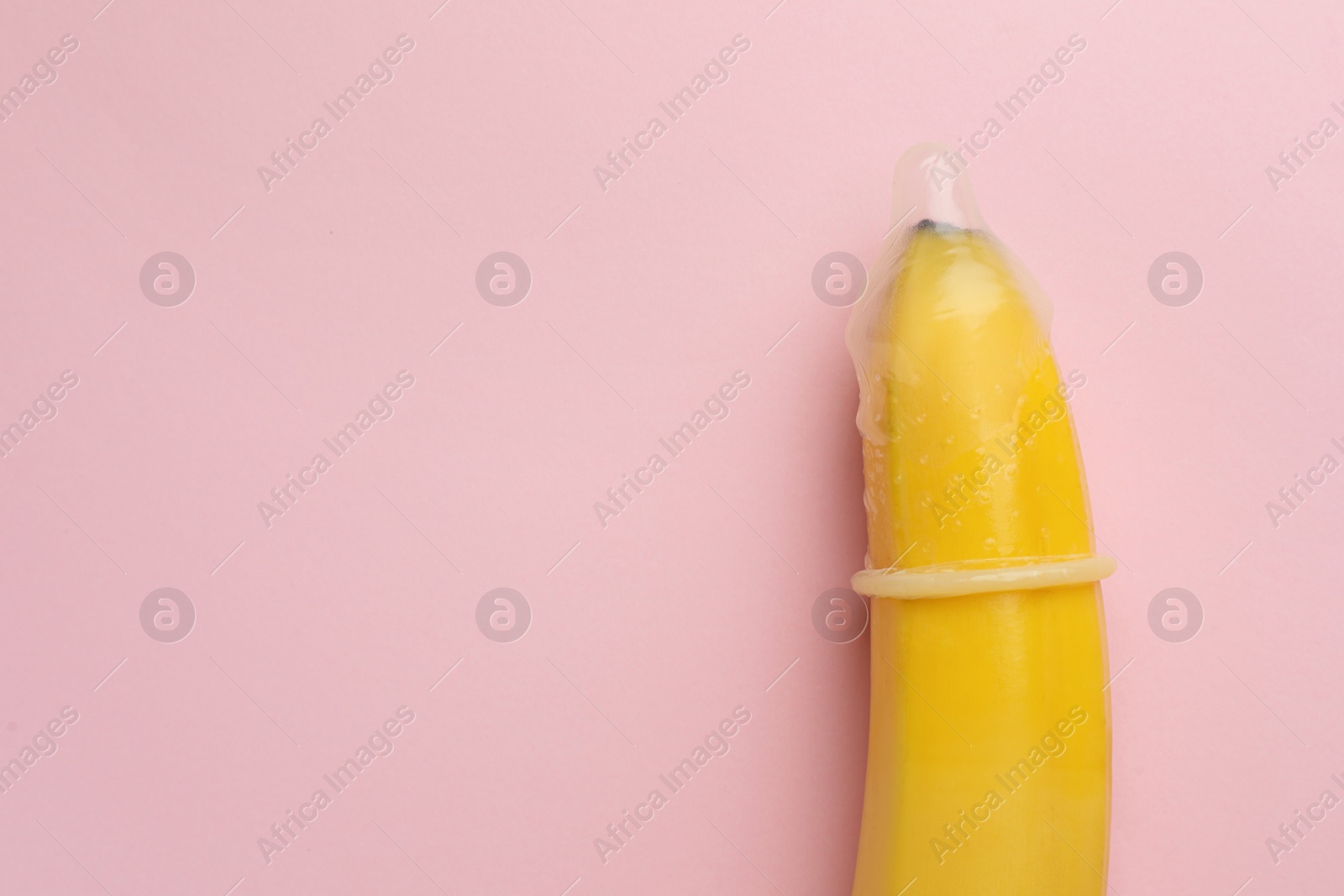 Photo of Banana with condom on pink background, top view and space for text. Safe sex concept