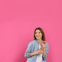 Young woman with glass of chocolate milk on pink background. Space for text