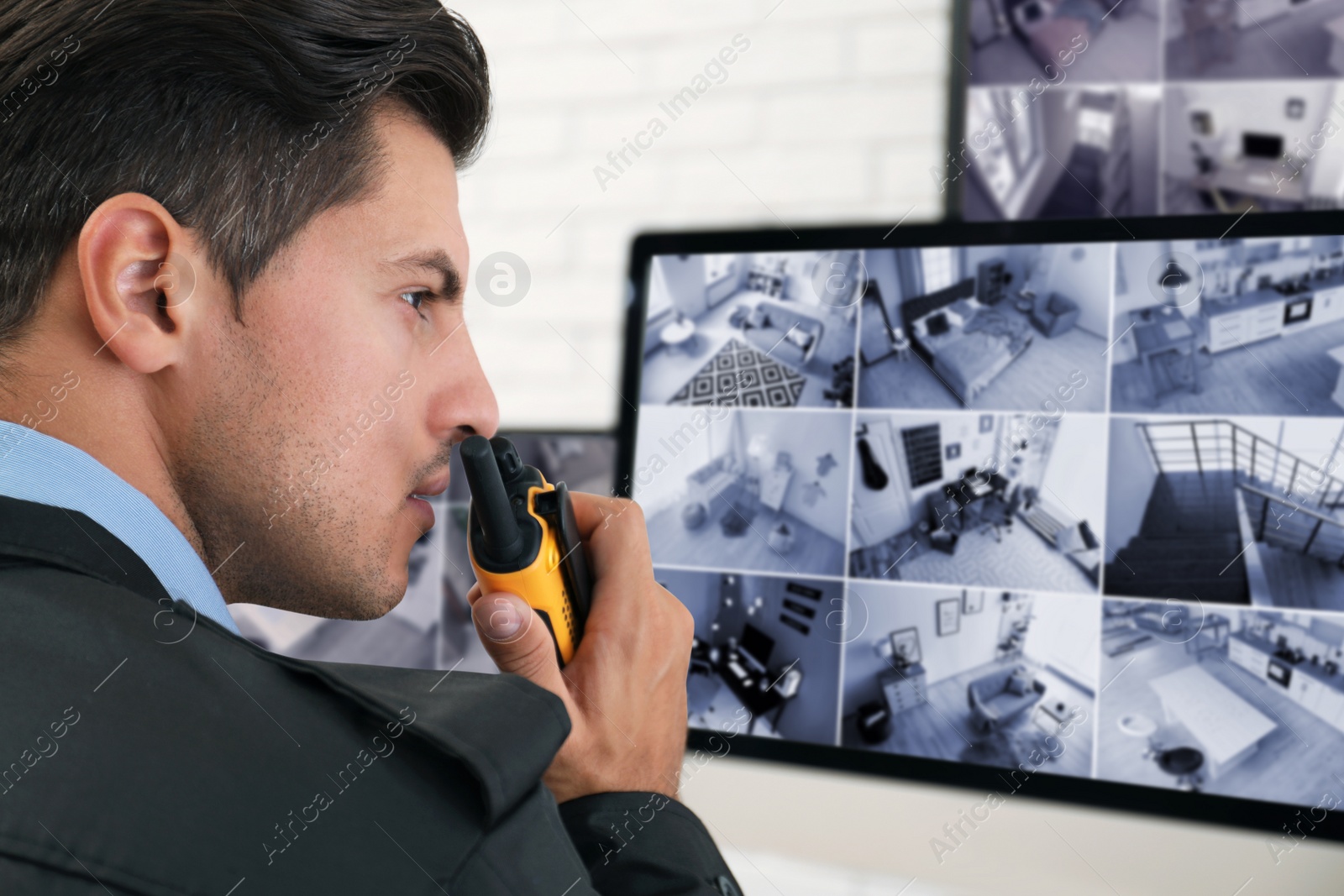 Photo of Male security guard with portable transmitter near monitors at workplace, closeup