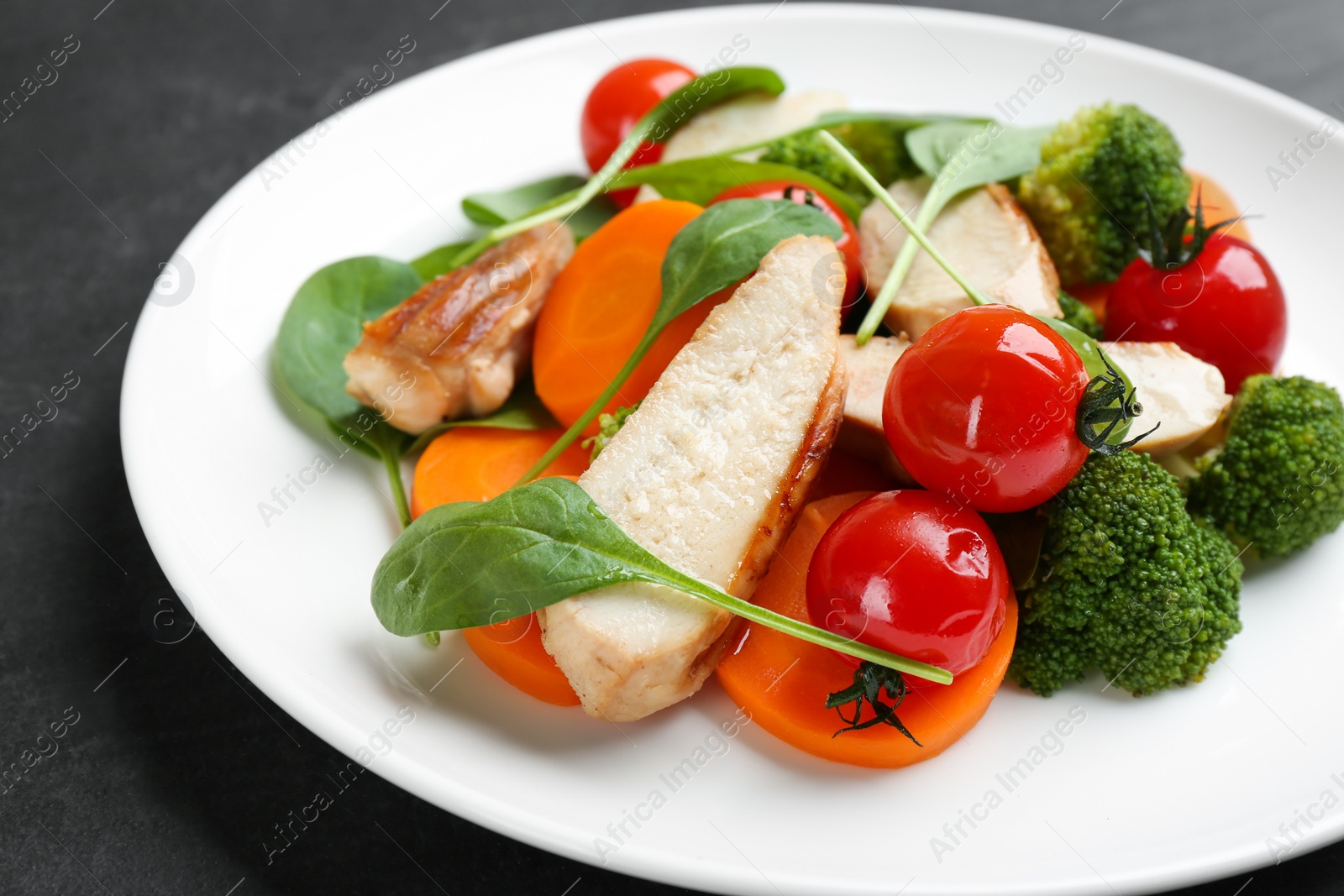 Photo of Delicious salad with chicken, vegetables and spinach on black table, closeup