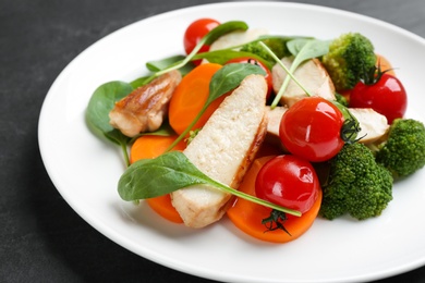 Photo of Delicious salad with chicken, vegetables and spinach on black table, closeup