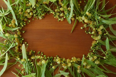 Photo of Frame of beautiful linden blossoms and green leaves on wooden table, flat lay. Space for text
