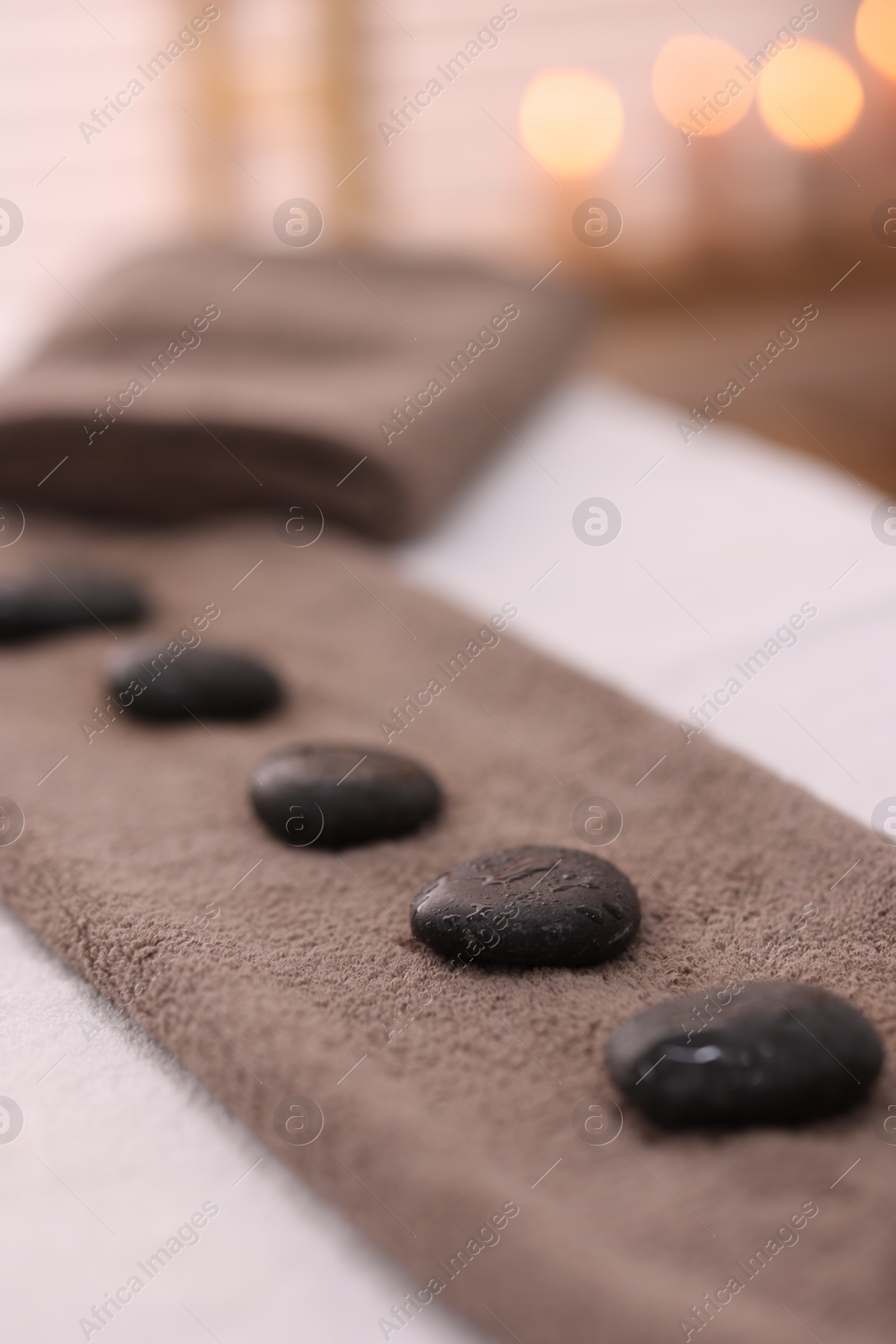 Photo of Towel with arranged spa stones on massage table in recreational center, closeup