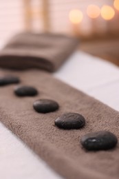 Photo of Towel with arranged spa stones on massage table in recreational center, closeup