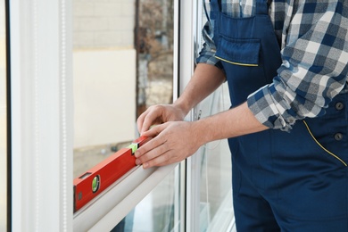 Construction worker using bubble level while installing window indoors, closeup