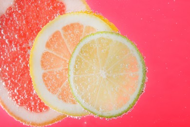 Slices of different citrus fruits in sparkling water on pink background, closeup