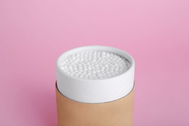 Container with new cotton buds on pink background