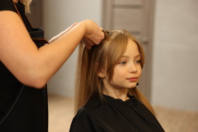 Professional hairdresser braiding girl's hair in beauty salon