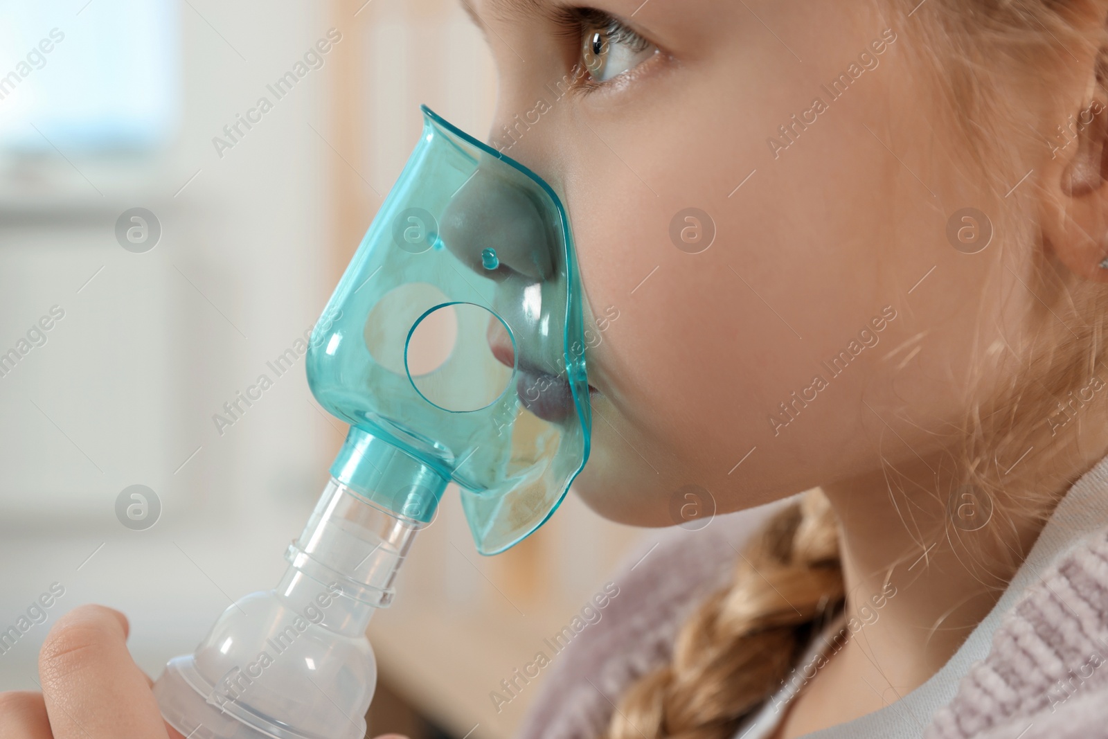 Photo of Little girl using nebulizer for inhalation indoors, closeup