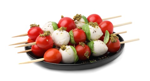 Photo of Plate of Caprese skewers with tomatoes, mozzarella balls, basil and pesto sauce isolated on white